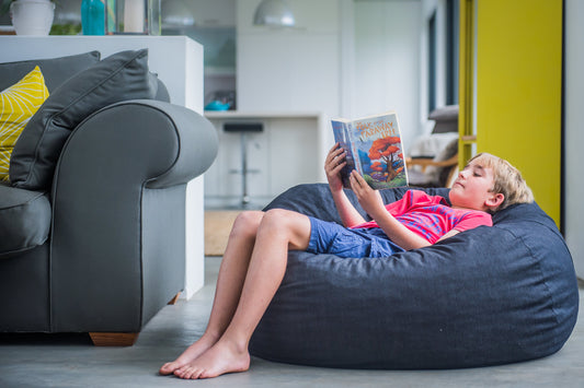 Boy reading a book on a denim Shloomfy foam beanbag that never goes flat