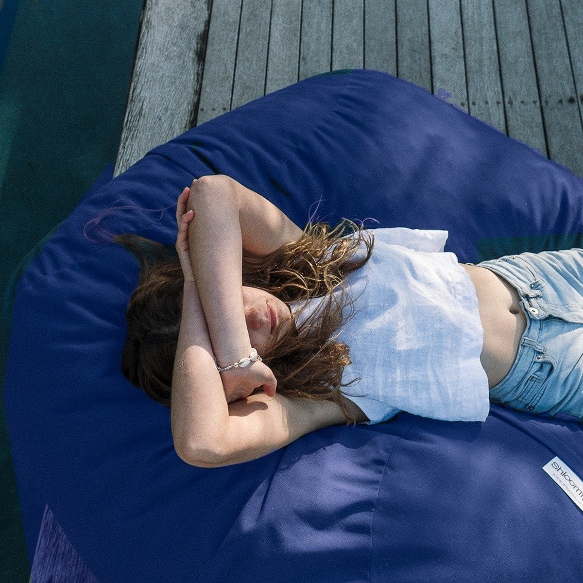 Girl lying on a Navy Shloomfy patio beanbag on a pool deck